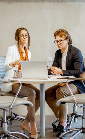 Young man and woman having a business conversation during the small conference, sitting at the round table in the meeting room