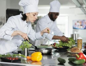 Food industry worker improving gourmet dish taste by adding fresh chopped basil, other herbs and